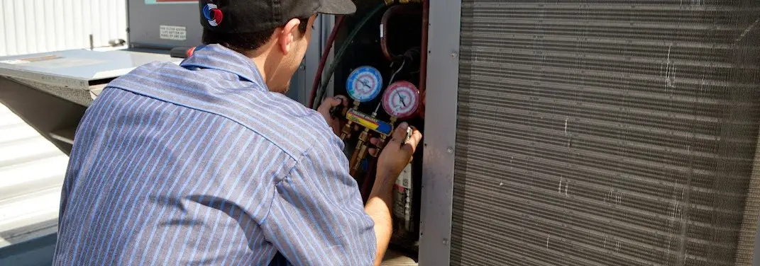 HVAC technician servicing a condenser unit in Canfield
